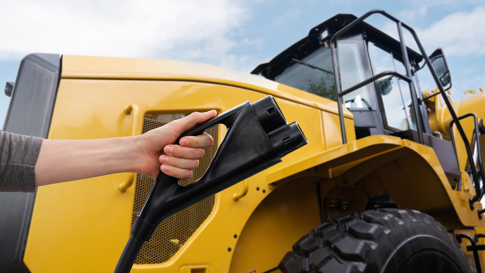 Hand with electric vehicles charging plug on a background of electric tractor